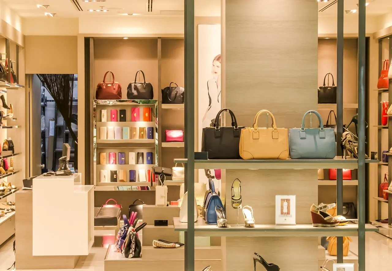 Ladengeschäft mit Handtaschen in Regalfächern über einer Ablage mit Damenschuhen, im Hintergrund weitere Taschen und Accessoires